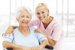 Portrait of happy female nurse with senior patient on wheelchair in nursing home. Horizontal shot.