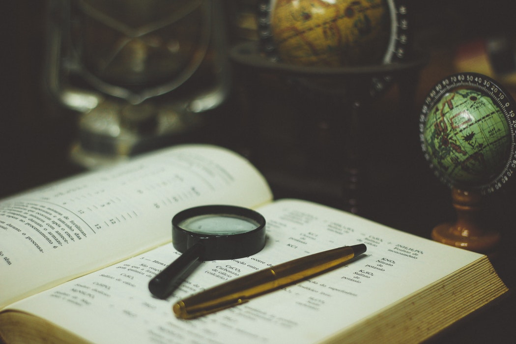 A magnifying glass and pen sitting on top of a book.